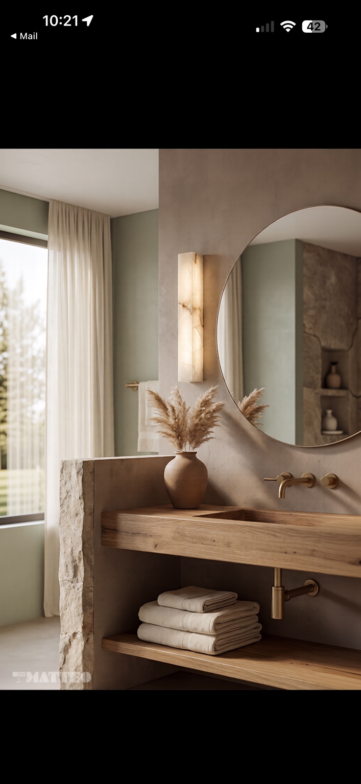 Warm modern bathroom with a round mirror, floating wood vanity and glowing rectangular stone wall sconce